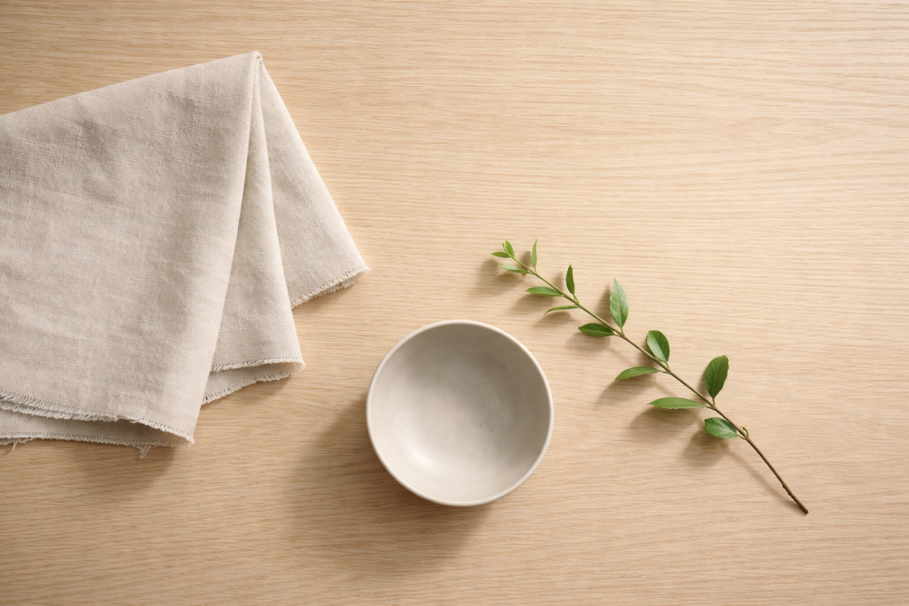 [light] Mission/værdier: symbolsk, rolig komposition med naturlige materialer (træ, lin, keramik) og en enkelt grøn gren. Bruges som visuelt anker ved værdier og redaktionelle principper.